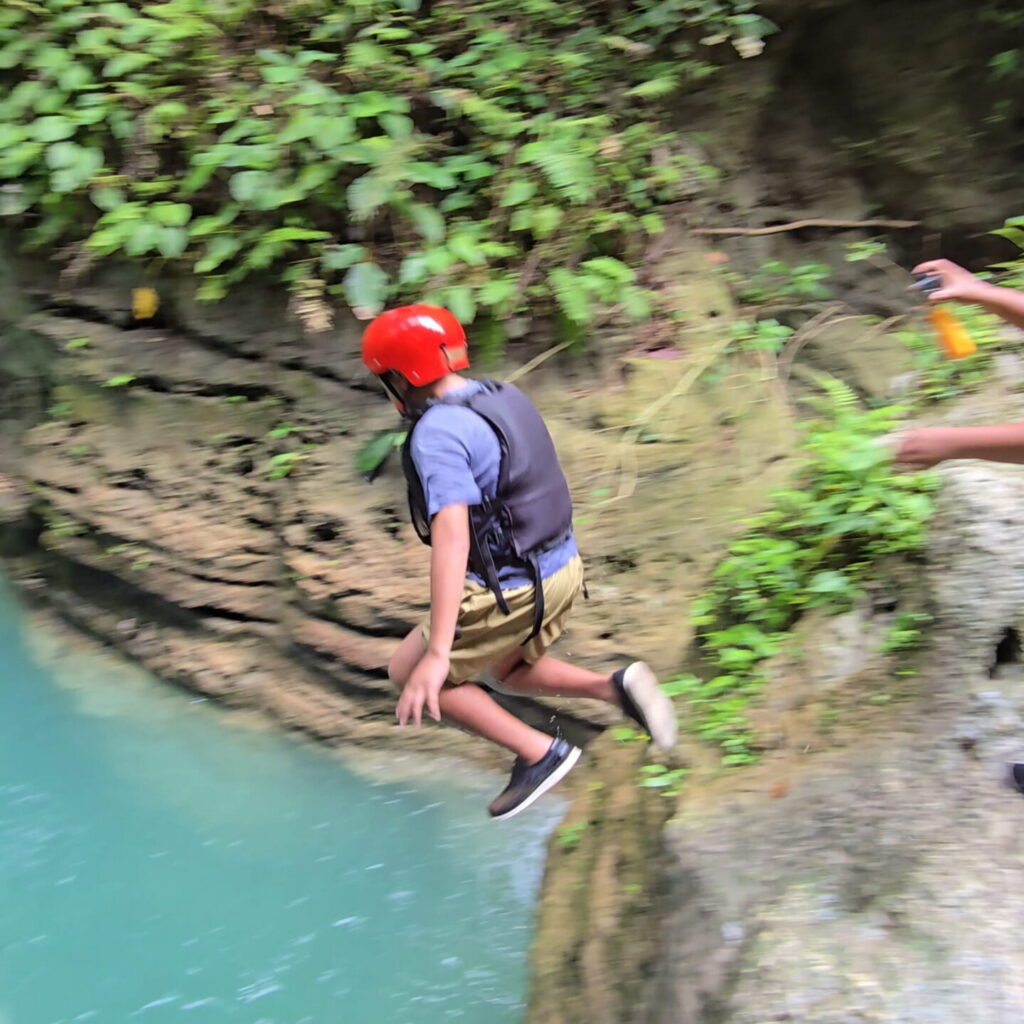 12-Year-Old Enjoying Kawasan Canyoneering in Badian, Cebu A 12-year-old child wearing a helmet and life vest jumps into the river during Kawasan Canyoneering in Badian, Cebu.