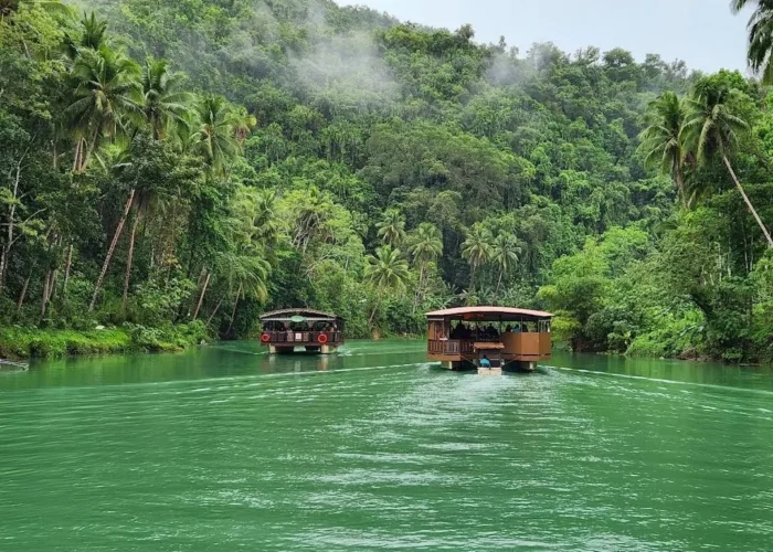 Floating restaurants cruising along the green Loboc River surrounded by coconut trees and tropical forest.