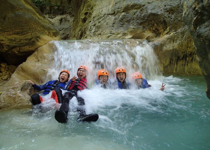 A group wearing helmets and life jackets enjoying a small waterfall during Kawasan canyoneering in Badian, Cebu.