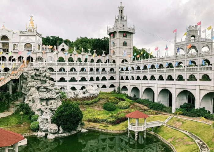 Wide view of the Monastery of the Holy Eucharist showing its towers, arched walkways, gardens, and pond.